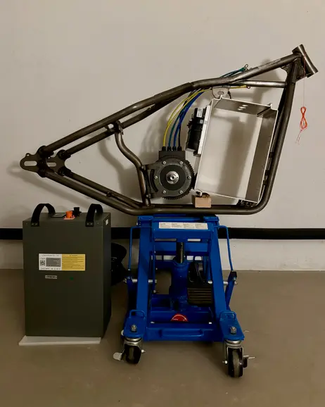 The frame up on a lift with the battery box on the floor beside it
