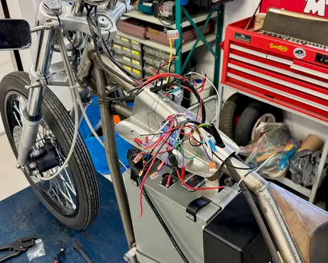 The bike on the lift with its wiring pulled out and laid over the frame