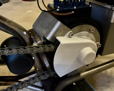 The updated front sprocket guard fitted over the drive, chain running below