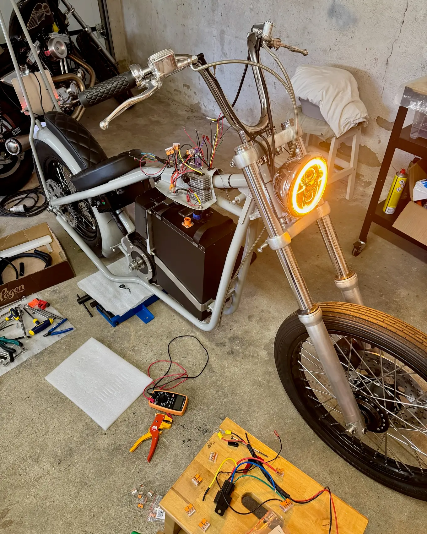The headlight lit in the dark garage, tools spread on the floor