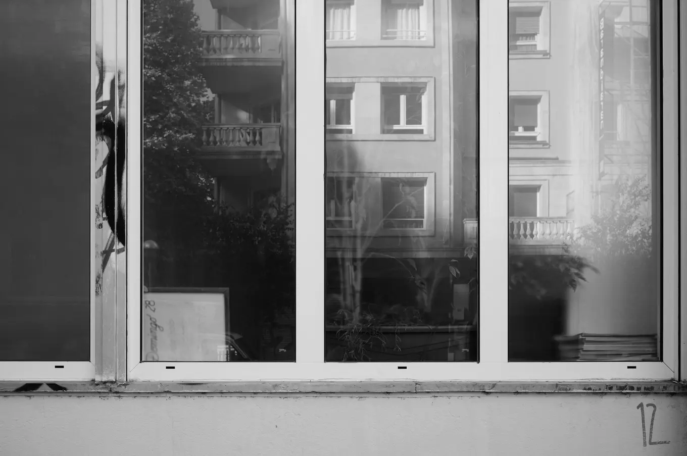 Apartment balconies reflected in the four panes of a shop window, the number 12 written on the wall below