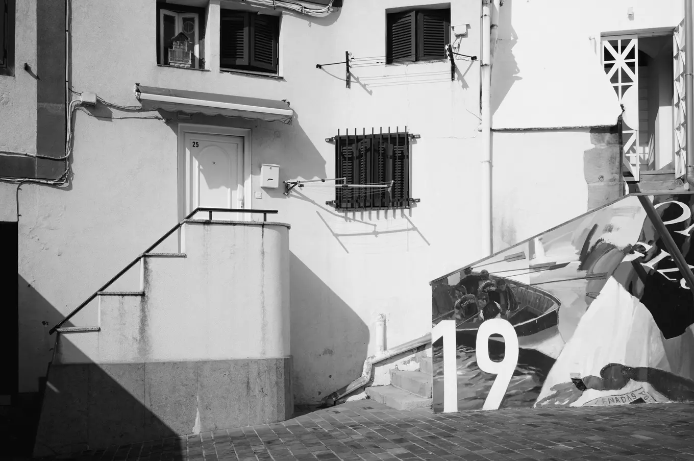 A whitewashed house with a stair to its door, a large advertising board with the number 19 leaning below it