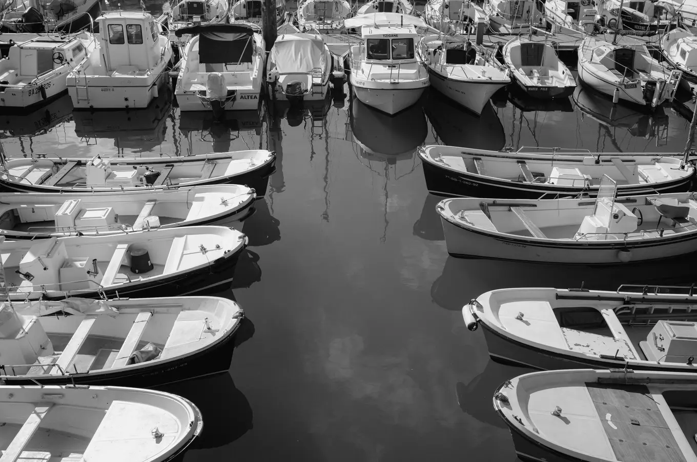 Rows of small open boats moored nose to nose in a harbour, cabin boats along the far quay