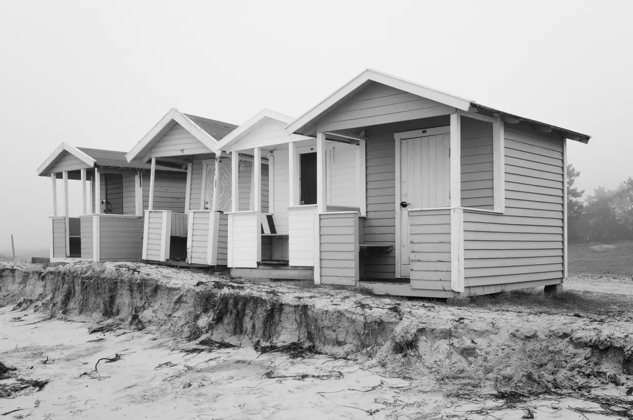 Four huts in a row along the top of an eroded sand bank