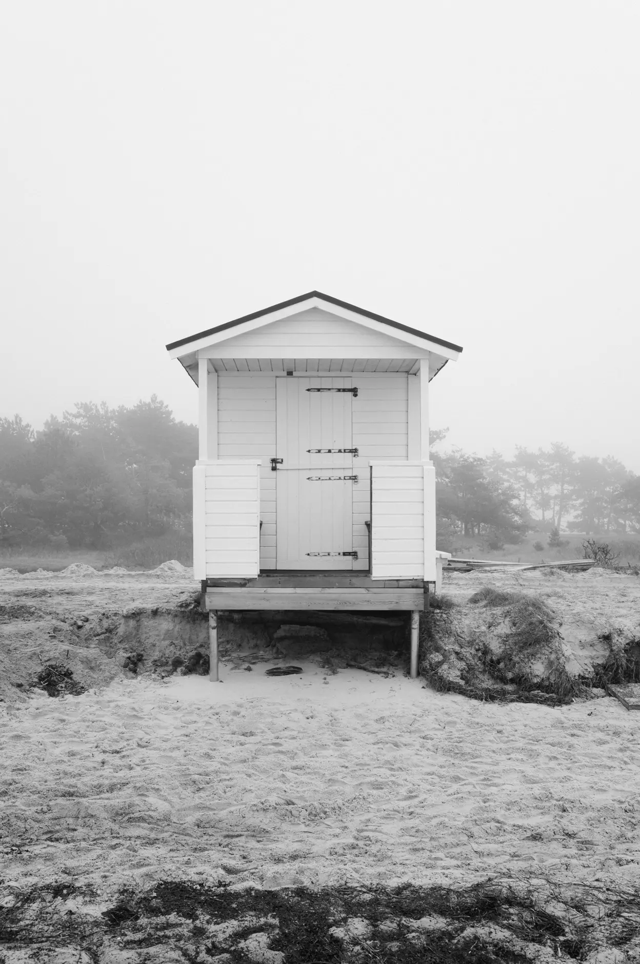 A white hut seen head on, its doors shut, the pine line faint behind it