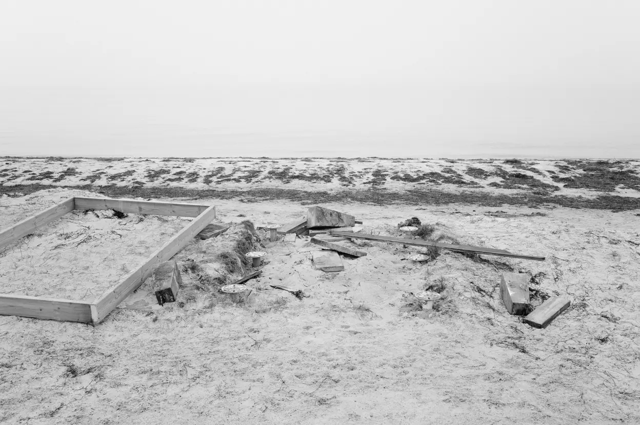 The bare foundation frame of a hut left in the sand, the sea flat behind it