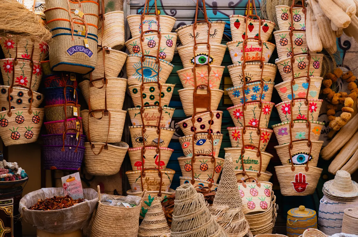 Rows of straw baskets hanging at a market stall, painted with eyes, flowers and strawberries