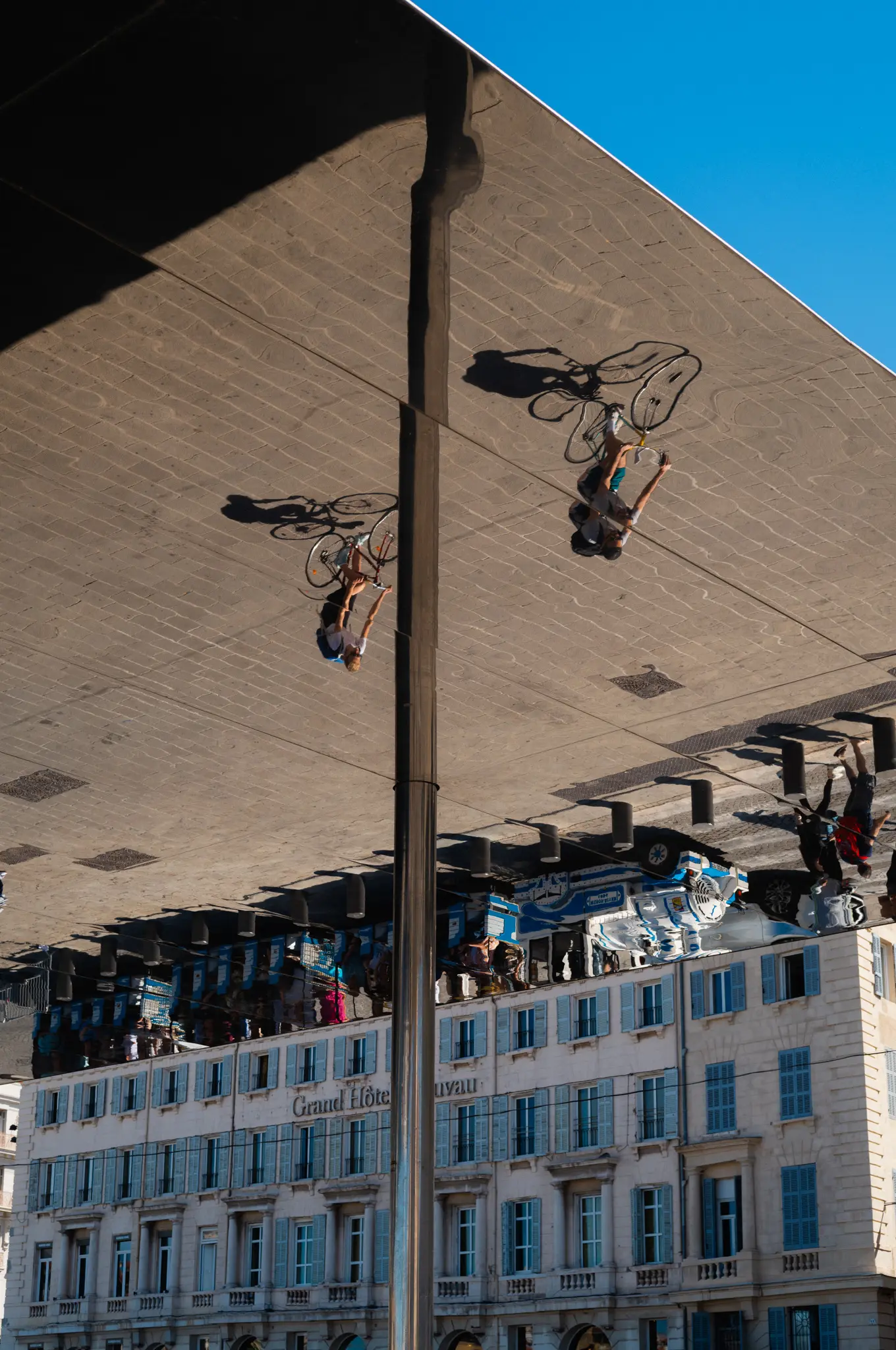 The mirrored canopy at the Vieux-Port reflecting cyclists and the buildings below it upside down, blue sky at the corner