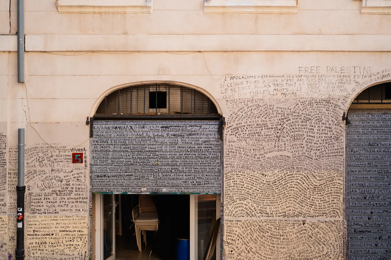 A shopfront and its arched doorways covered from edge to edge in handwritten text, stacked chairs inside the open door