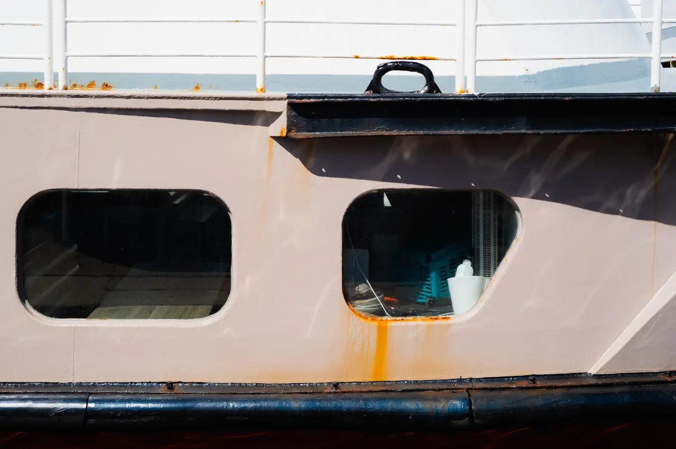 Two rounded portholes in a rust-streaked hull, a blue crate and a white bottle visible through one of them