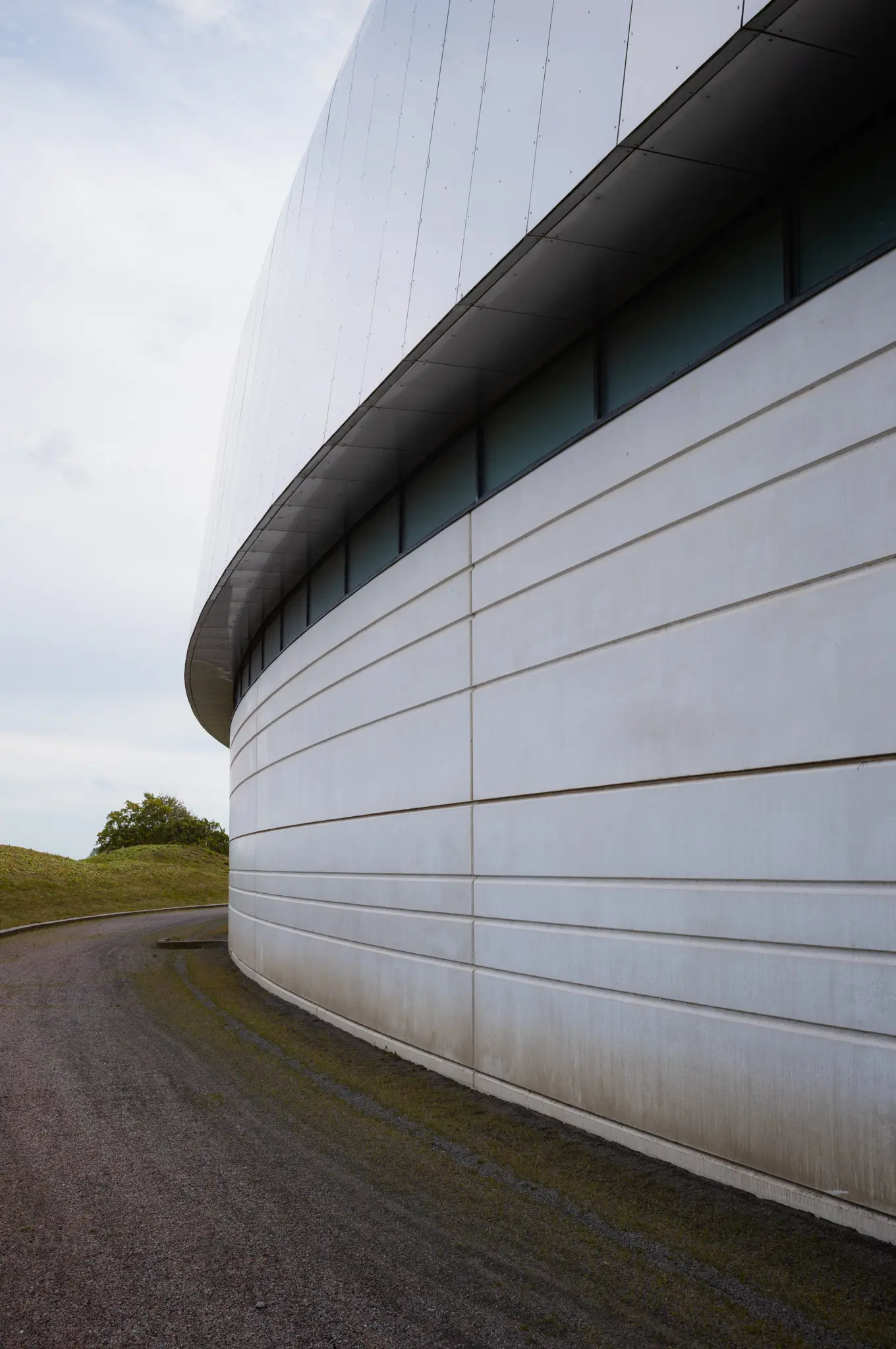 The curved wall of the ring hall following a gravel path