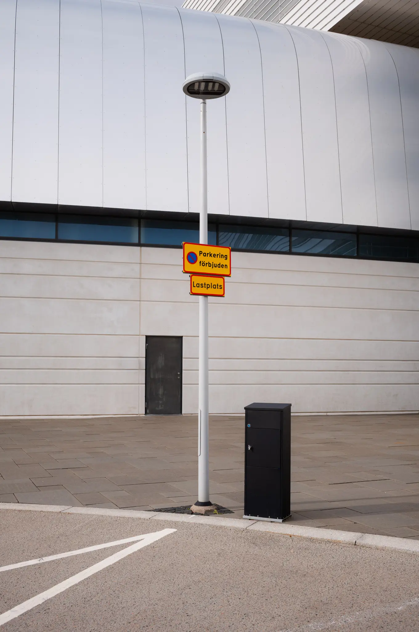 Parking signs on a lamp post at a loading bay, the curve of the ring hall behind