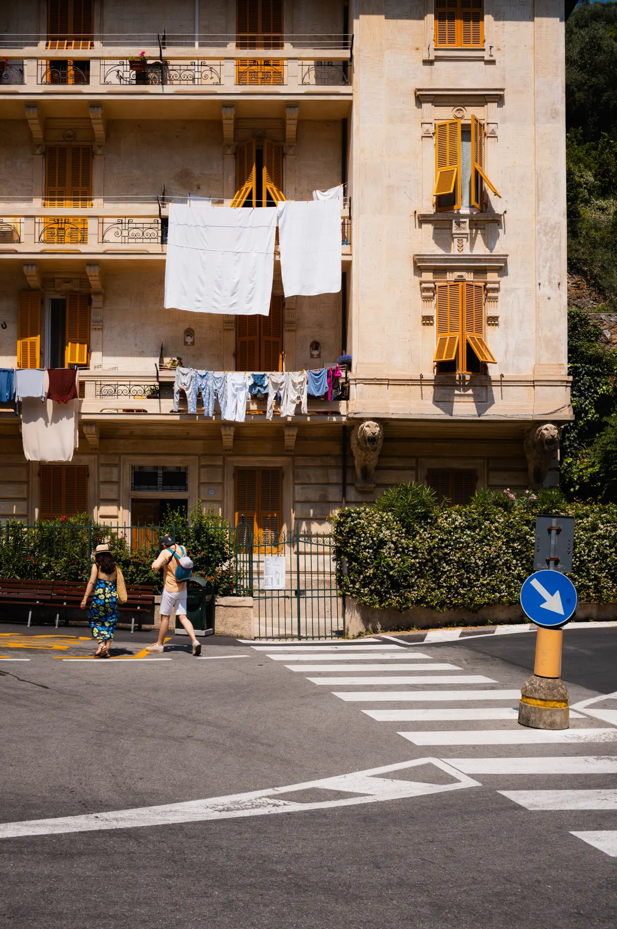 Sheets drying on a balcony above a crossing, two people walking under them