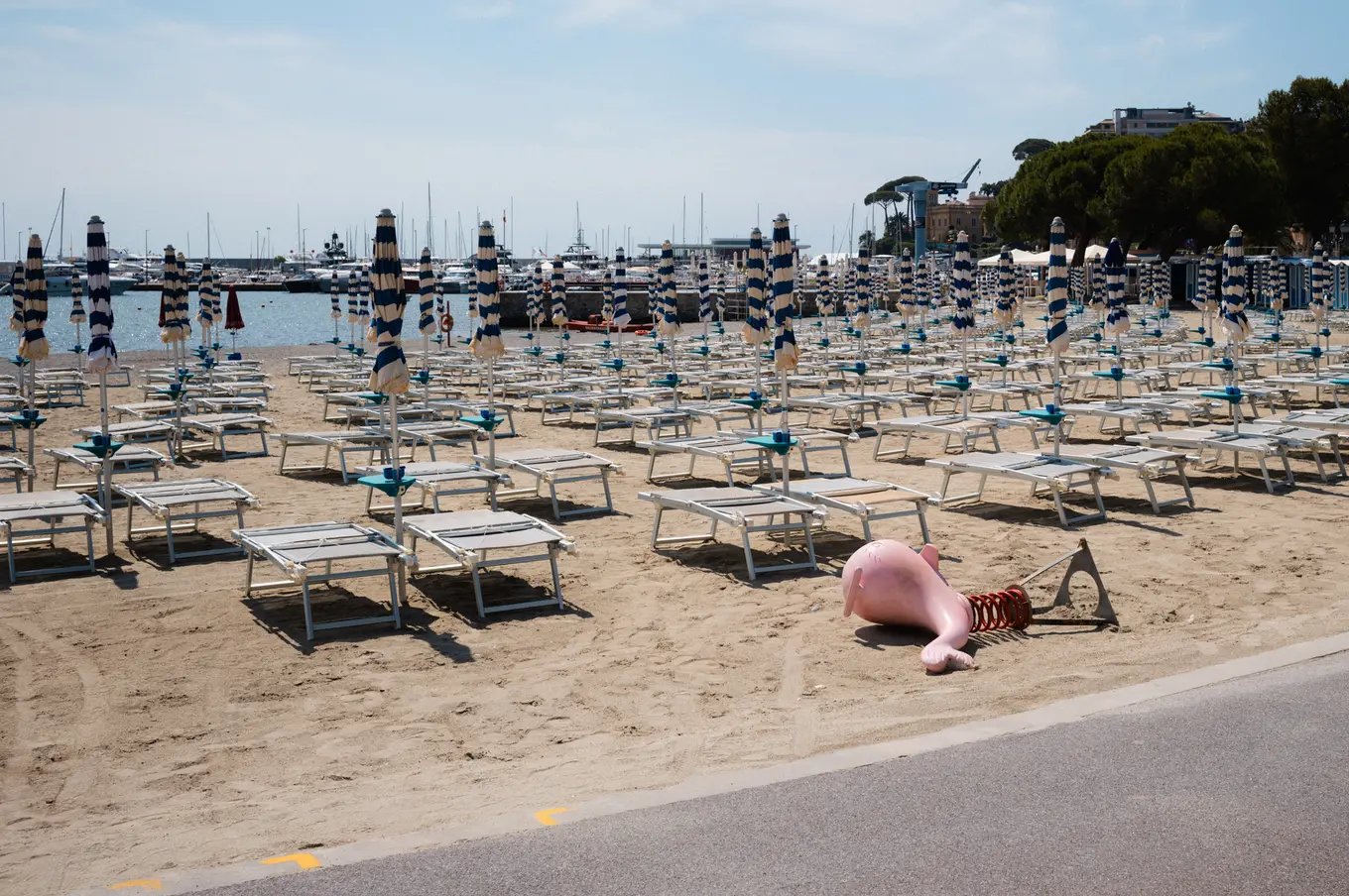 Rows of empty loungers and folded parasols on a beach, an inflatable left on the sand