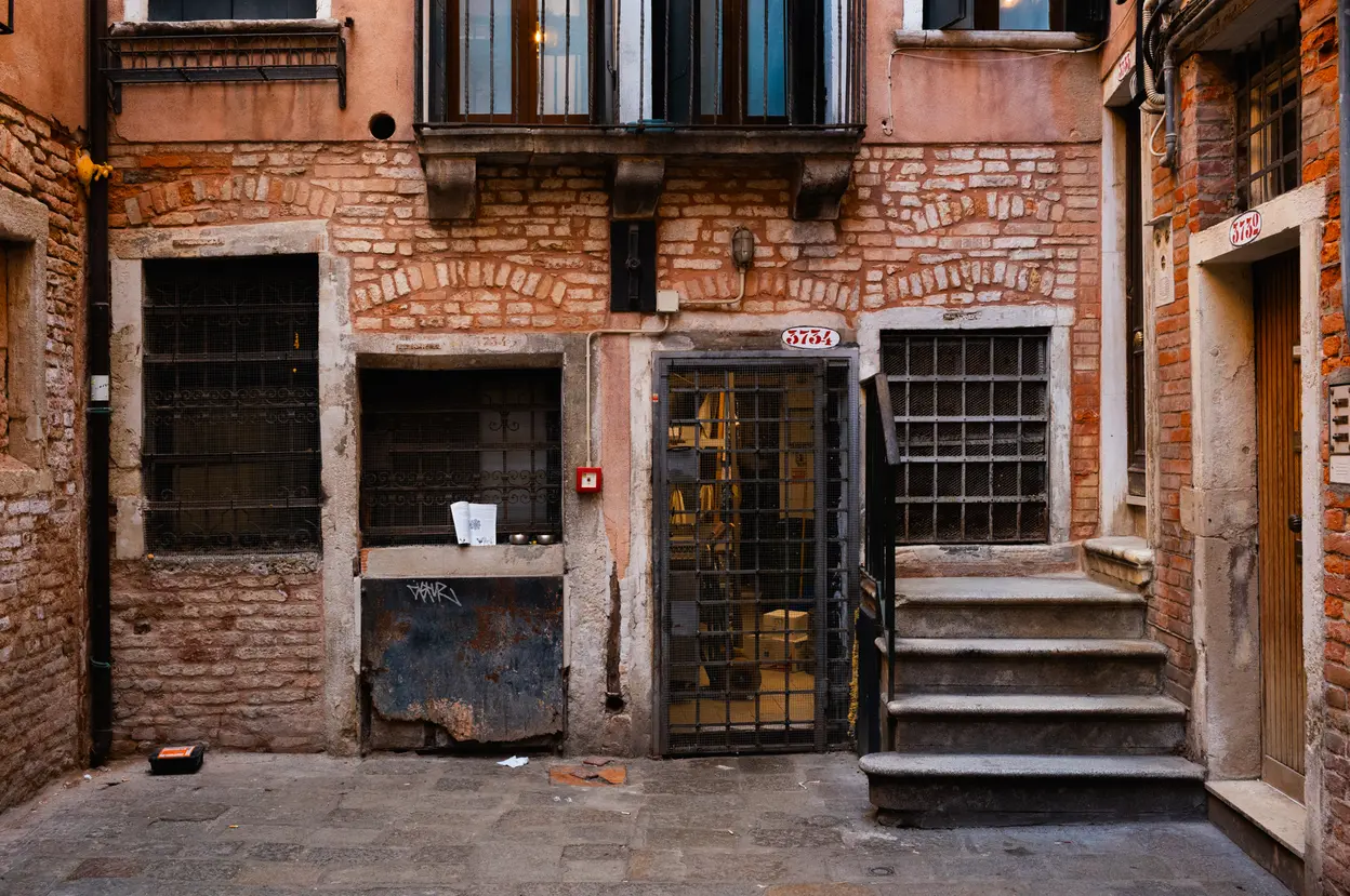 A brick courtyard with barred doors and a worn stone staircase